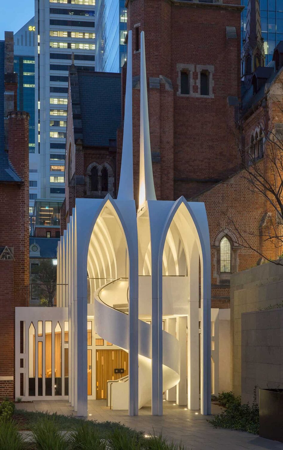 Illuminated white contemporary chapel facade beside a heritage brick building, Perth city