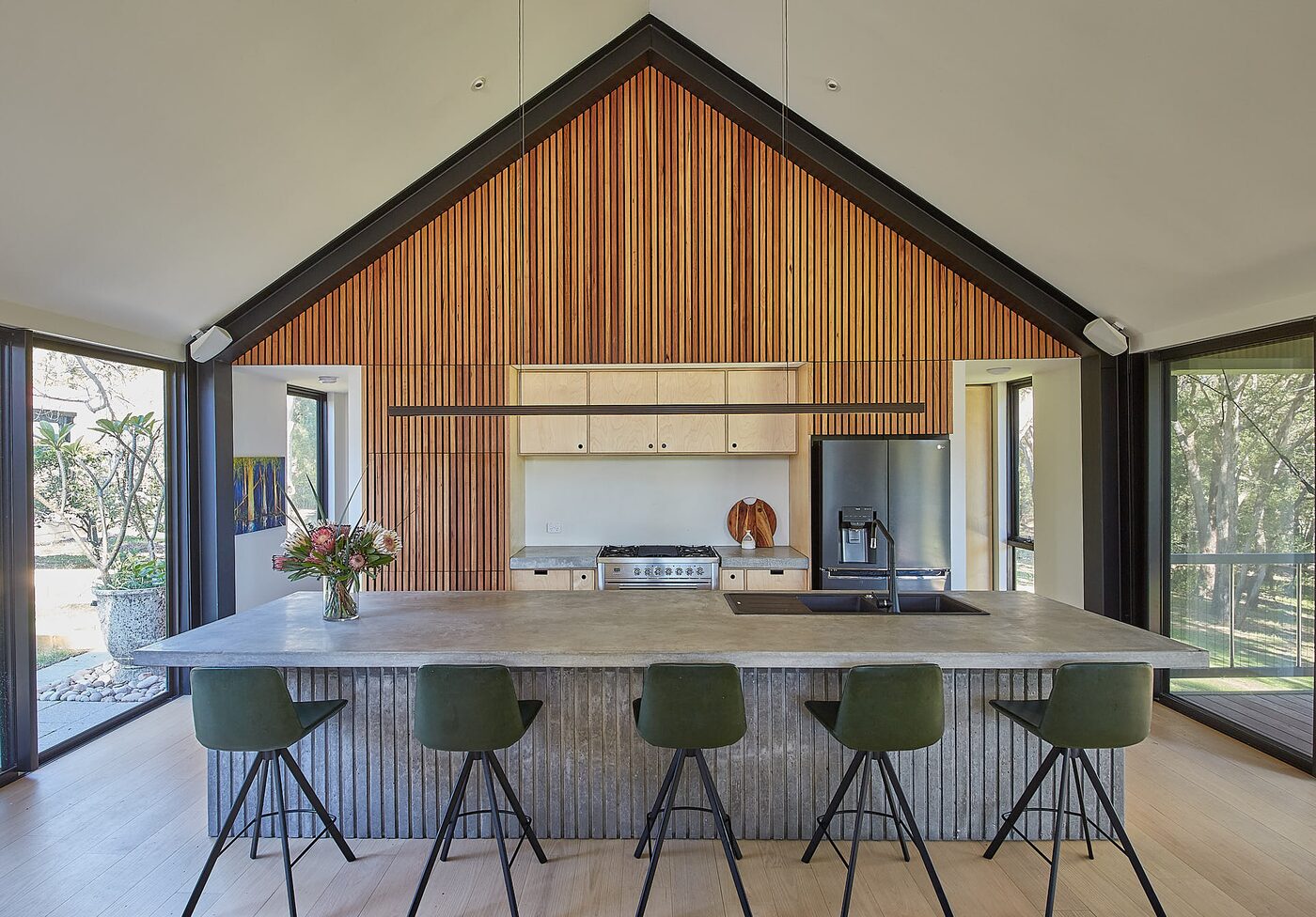 Kitchen under a raked timber ceiling with island bench and green stools