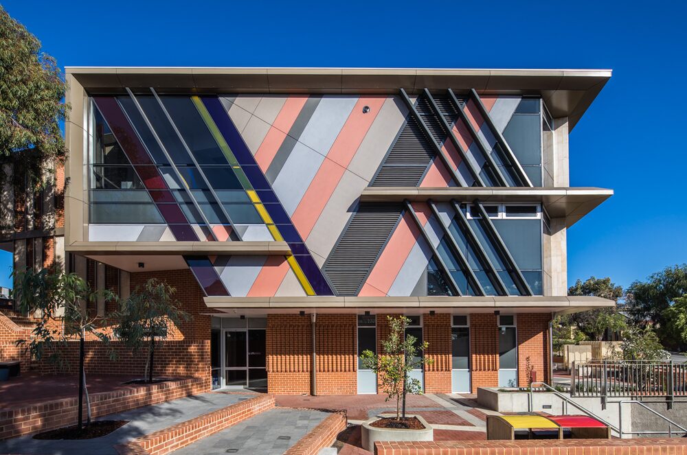 Three storey building with a bold striped facade above a brick forecourt